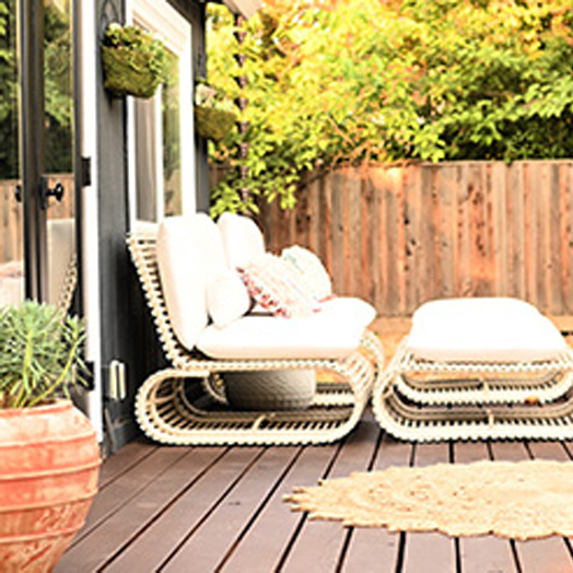 A brown deck with white cushioned furniture, a floor plant, and a feature rug.